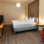 Geräumiges Premium-Zimmer im B&B Number 1 Bad Loipersdorf mit Boxspringbett, Relax-Sessel und Tisch für vielseitige Nutzung.