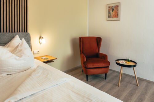 Premium-Zimmer im B&B Number 1 Bad Loipersdorf mit Boxspringbett, gemütlichem Sessel und modernem Beistelltisch.