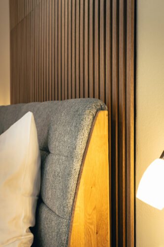 Detailaufnahme eines stilvollen Boxspringbetts mit grauem Polster und Holzlamellen-Wandelement im Premium-Zimmer des B&B Number 1 Bad Loipersdorf.